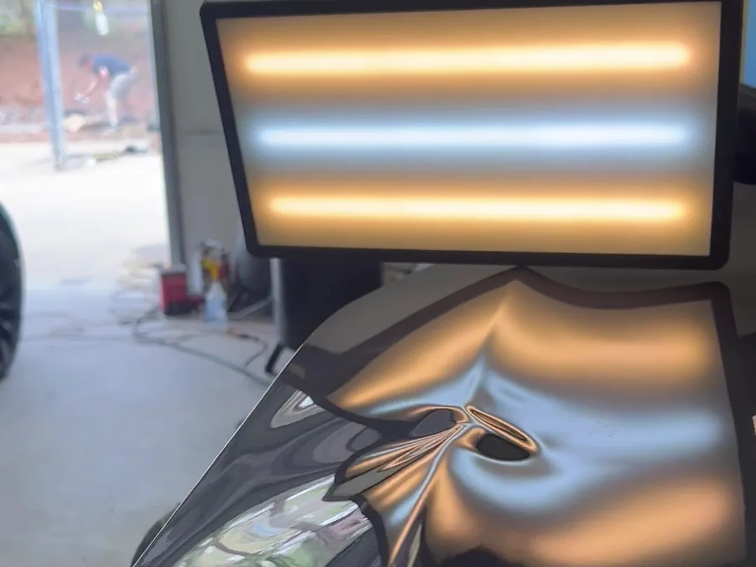The dent board reflected across a black panel, the light bending around a dent